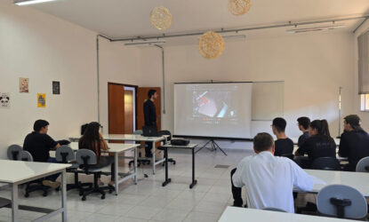 Na fotografia há uma sala com projeção numa tela branca em que um ministrante apresenta informações para um público de sete ouvintes sentados e olhando para tela.