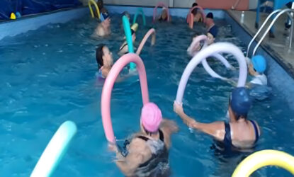 A fotografia mostra pessoas em uma piscina realizando exercícios aquáticos.