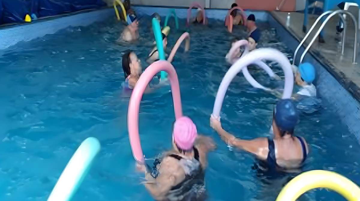 A fotografia mostra pessoas em uma piscina realizando exercícios aquáticos.