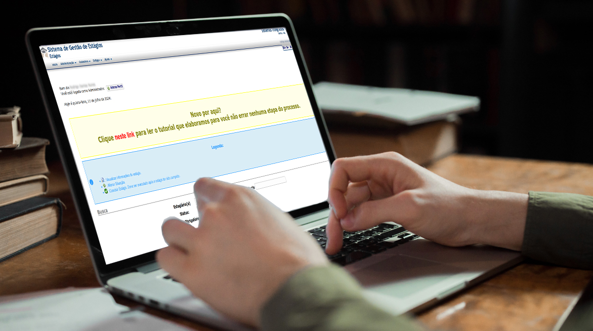A imagem é uma fotomontagem que mostra uma tela de notebook com a página web do Sistema de Estágios e e à frente, as mãos de um homem digitando. No segundo plano, aparecem livros sobre a mesa atrás do notebook.