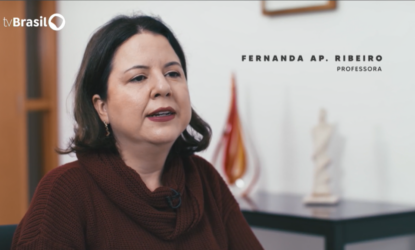 Na imagem, está a docente Fernanda, em enquadramento fechado, isto é, representada até os ombros. A professora está com os lábios vermelhos de batom e uma camisa vinho. Atrás dela há uma mesa com duas esculturas. Do lado superior esquerdo, há o Logo da TV Brasil e, no canto superior esquerdo, estão os escritos "Fernanda Ap. Ribeiro Professora". Fim da descrição
