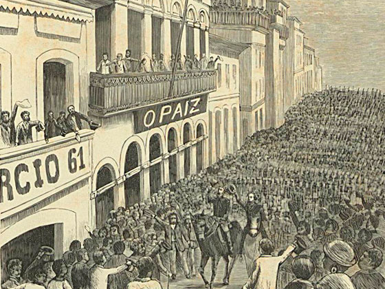 A imagem é uma ilustração histórica em tom sépia retratando a ovação popular ao marechal Deodoro da Fonseca e a Quintino Bocaiúva, na Rua do Ouvidor, no Rio de Janeiro, em decorrência da Proclamação da República. Várias pessoas estão reunidas nas sacadas e janelas, enquanto uma multidão densa ocupa toda a rua. No centro, dois cavaleiros passam entre a multidão, sendo o foco da atenção. 