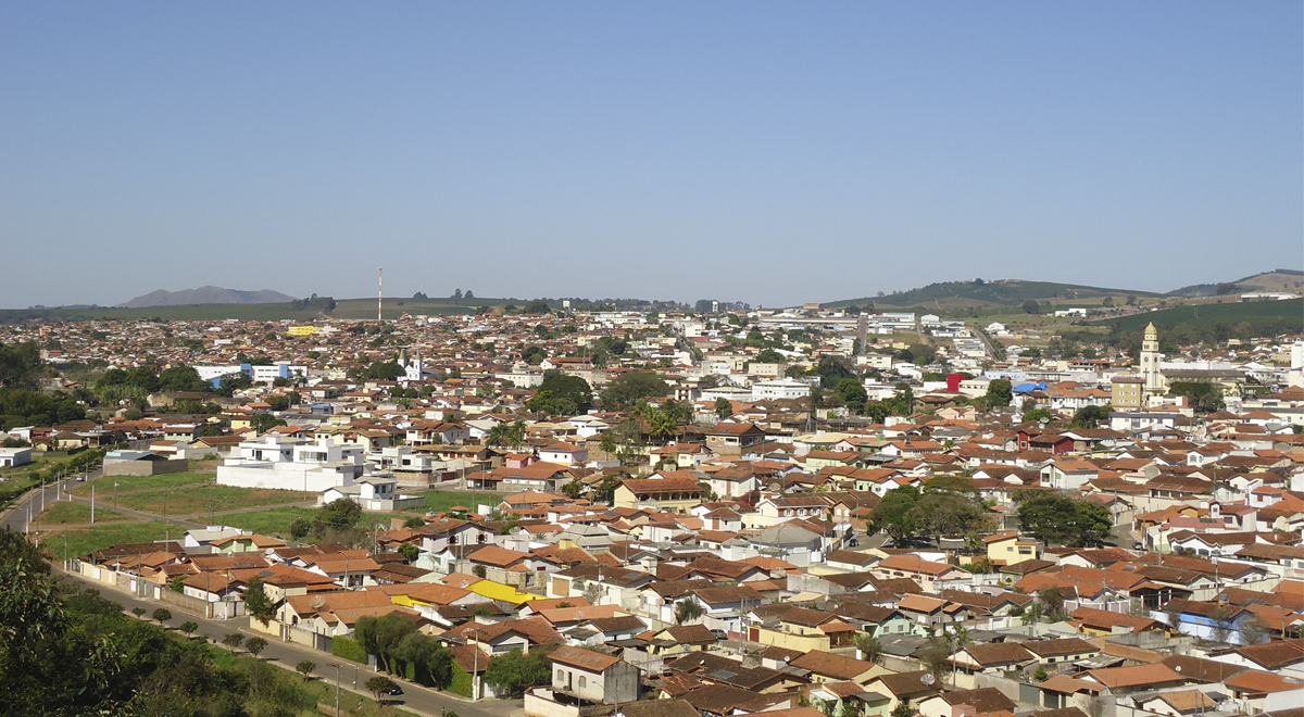 A imagem mostra uma foto da cidade de Três Pontas-MG, com parcial aérea da cidade, na qual dá para ver a Igreja Matriz Nossa Senhora da Ajuda à direita e, ao fundo à esquerda, a Serra de Três Pontas.